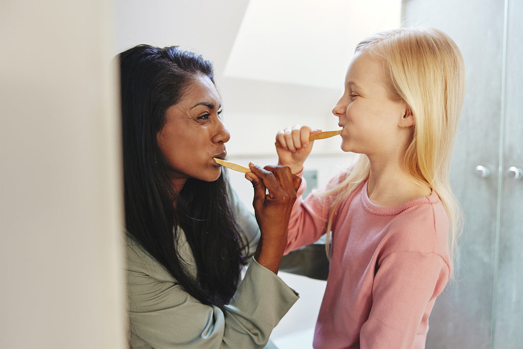 A woman and a child brushing teeth together looking into each others eyes